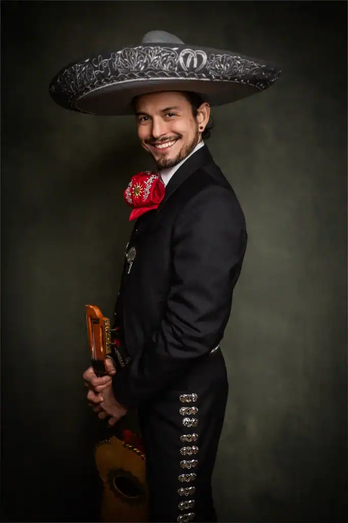Man in traditionele Mariachi-kleding met grote sombrero, lachend en met gitaar, promotie voor Mariachi Los Tarascos optredens op woensdagavond.