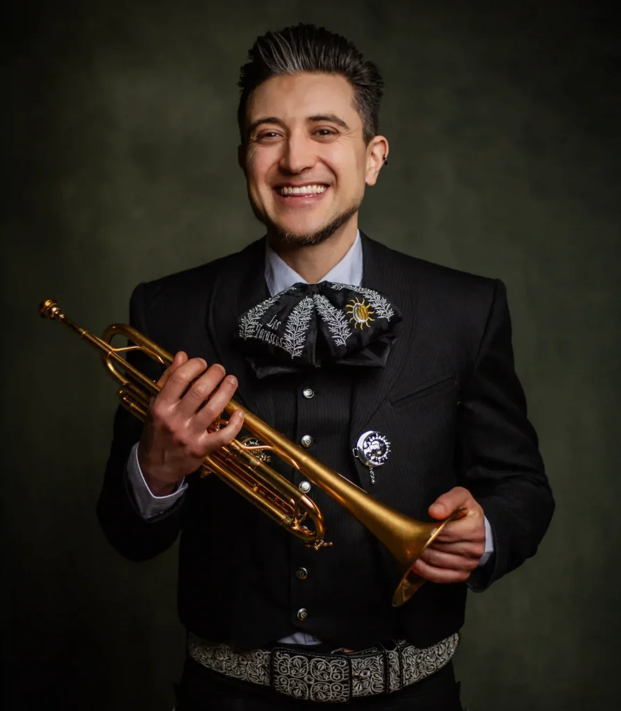 Gelukkige mariachi muzikant met trompet, gekleed in traditioneel mariachi kostuum, tijdens optreden bij Las Mañas, met een donkere achtergrond.