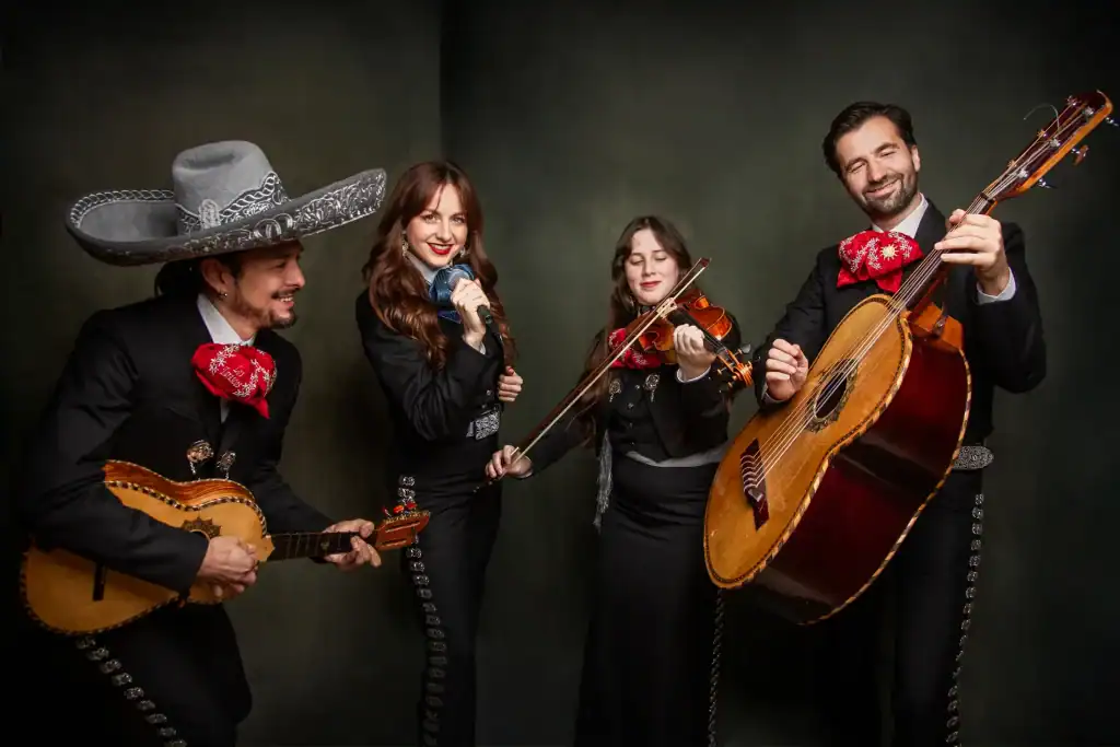 Mariachi Los Tarascos in traditionele kleding met gitaren en violen, optredend voor een publiek, onder de titel "Mariachi Los Tarascos: Elke woensdagavond".