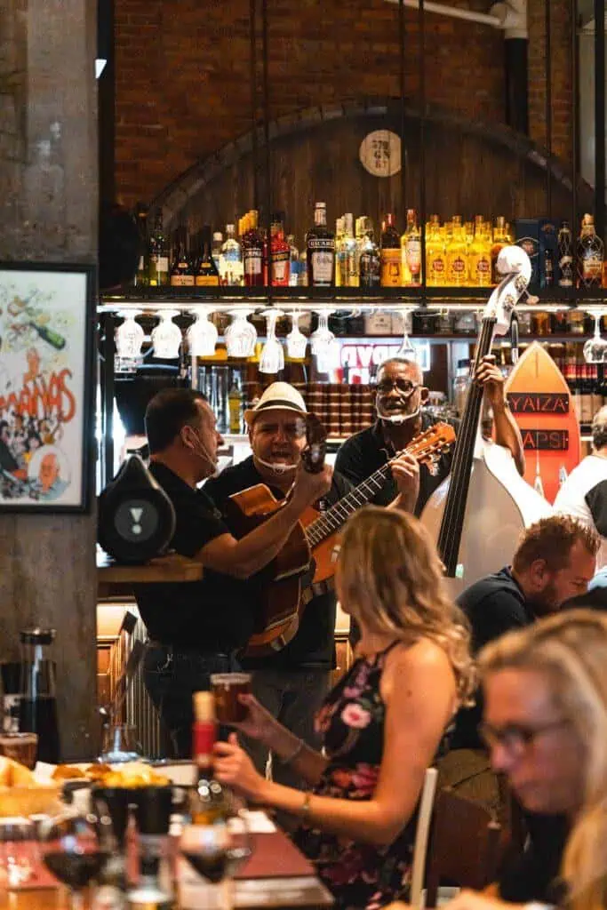 Kamers met live flamencomuziek in een sfeervol Spaans restaurant, bar met gezellige ambiance, duidelijk zichtbare bar met verschillende drankjes, muzikanten met gitaar en contrabas, ideale locatie voor genot en ontspanning.