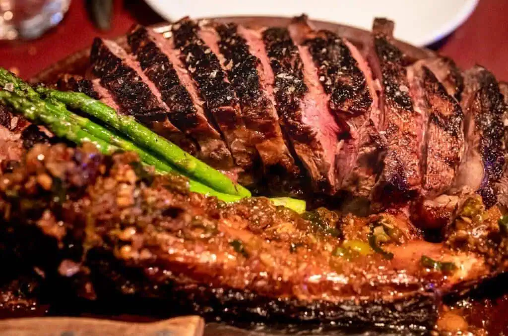 Steak grillé juteux et asperges vertes croustillantes servis sur une assiette en bois à Las Mañas, un restaurant de tapas de premier plan en Belgique, connu pour ses spécialités méditerranéennes et son atmosphère chaleureuse.