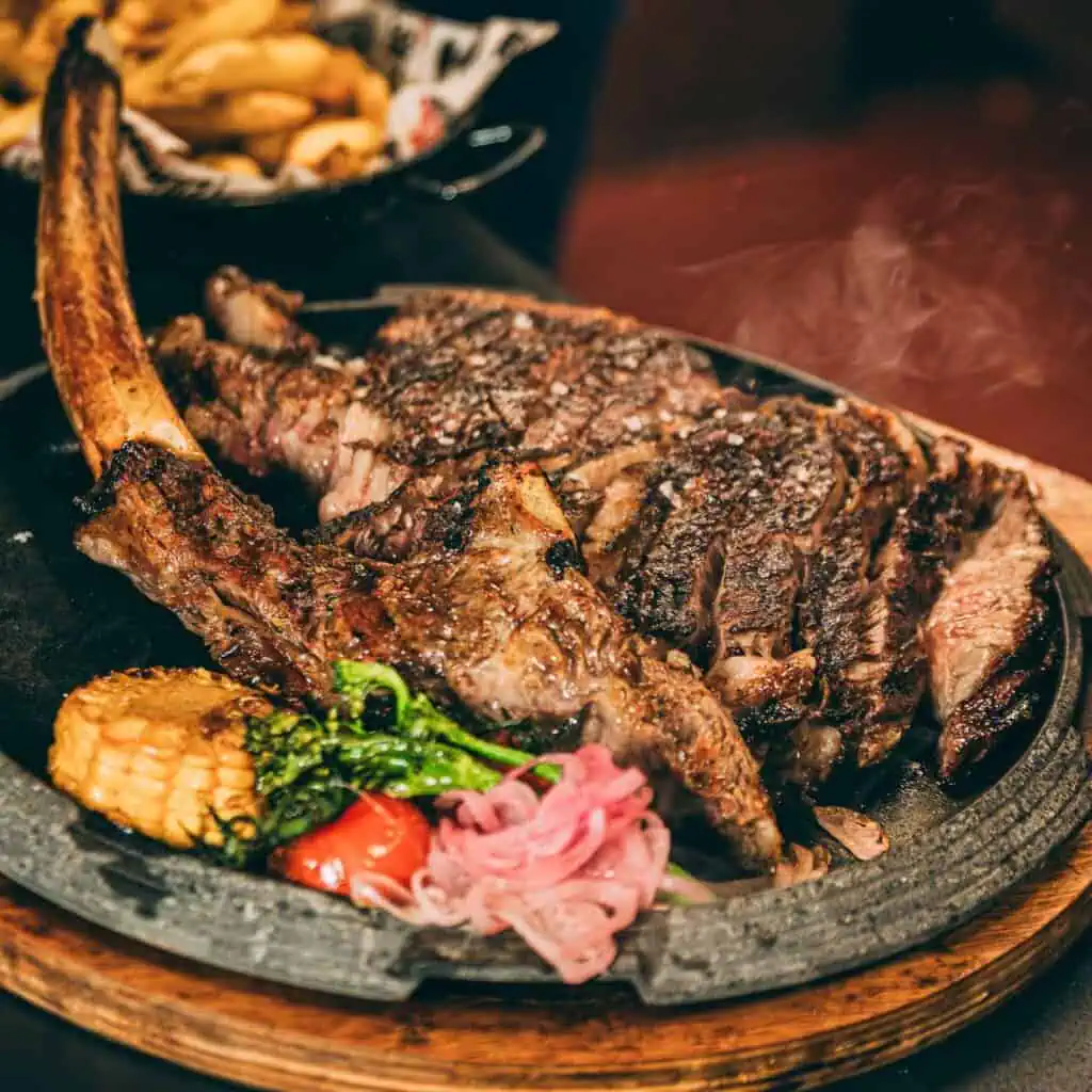 Steak d'aloyau américain mariné avec des légumes grillés et des herbes, servi sur une assiette en pierre chaude. Parfait pour les amateurs de viande qui apprécient l'expérience authentique des tapas à Las Mañas.
