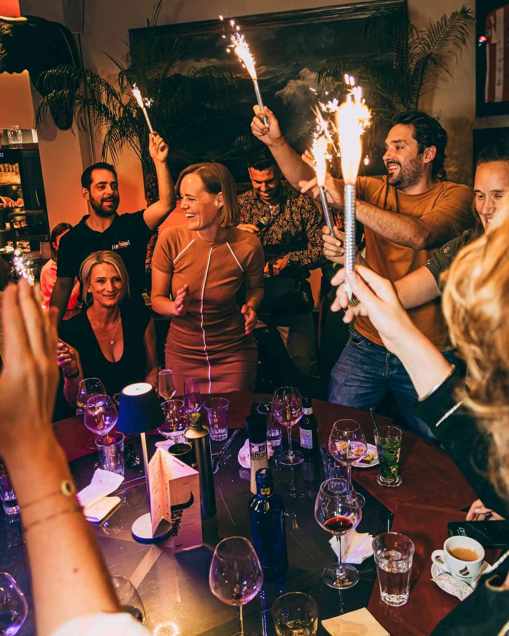 Ambiance de fête chaleureuse avec des personnes célébrant un anniversaire ensemble, avec des boîtes de confettis et du champagne, dans un restaurant atmosphérique au décor coloré.