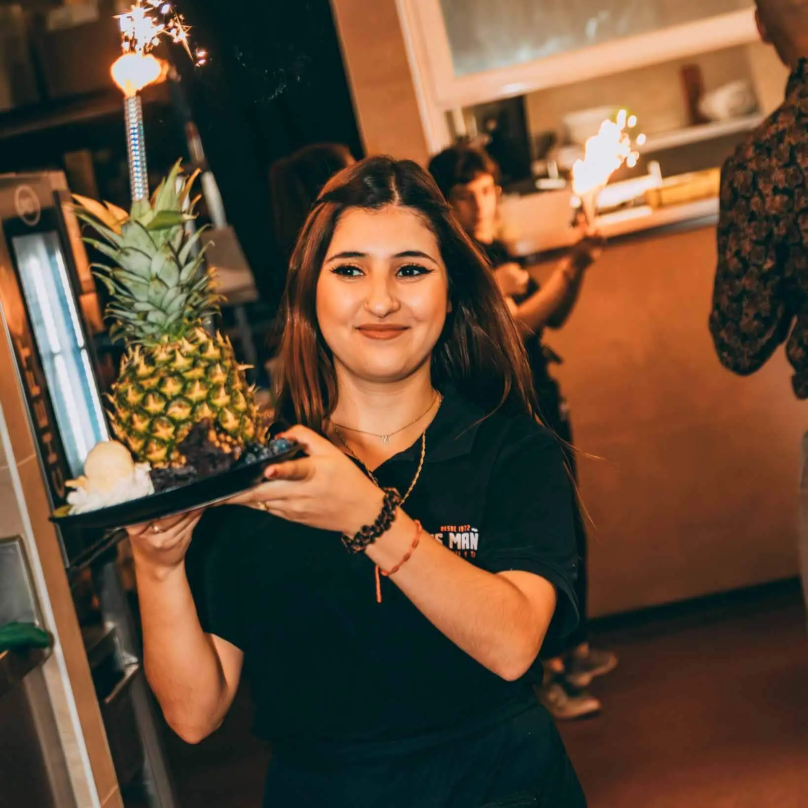 Prachtige serveerster met tropische ananas en bessen bij Las Mañas, vrolijke sfeer in restaurant, gastvrijheid en culinaire presentatie, catering en feestelijke gelegenheid, tropisch en modern interieur.
