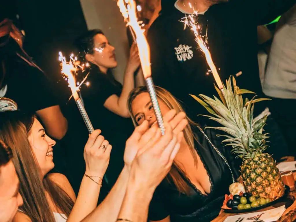 Rassemblement festif avec des personnes dégustant du champagne et des articles de fête, notamment des feux d'artifice et des fruits frais, pour une impression d'ambiance joyeuse et festive.