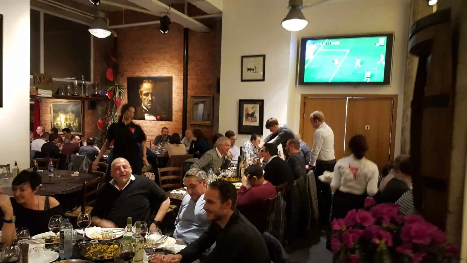Gezellige Spaanse tapasbar Las Mañas in Antwerpen met drukke sfeer, waar gasten genieten van authentieke tapas en wijn. Het interieur is versierd met kunstwerken en biedt een gezellige ambiance voor een leuke avond uit.