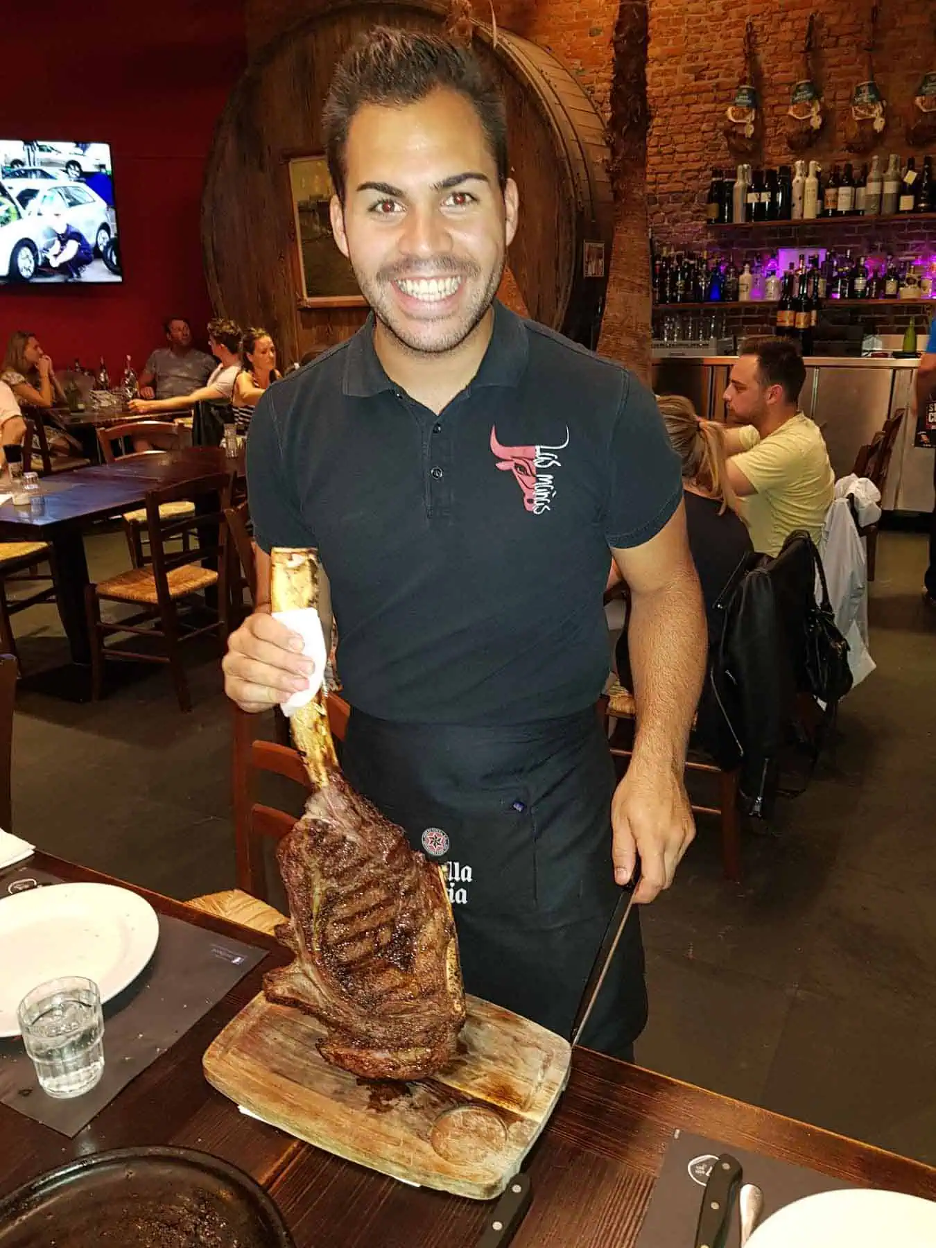 Robuuste portie steak in La Mañas restaurant, sfeer van een gezellig Belgisch eetcafé met warme rode en bruine tinten, drukke bijeenkomst met gasten die genieten van heerlijke biefstukken.
