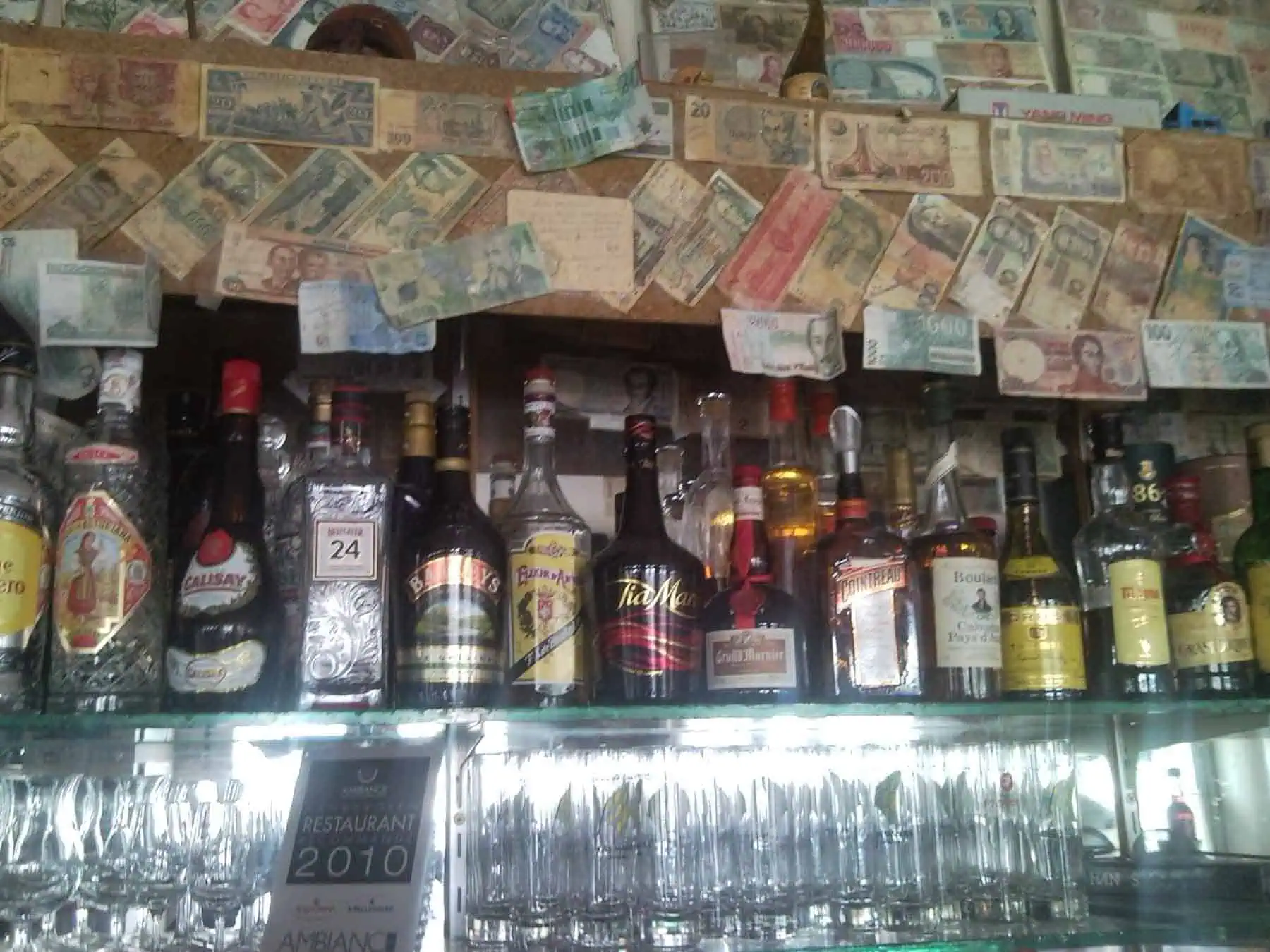 Gezicht op de bar met diverse flessen drank en een overvloed aan bankbiljetten, mogelijk als decor of voor een speciale gelegenheid, in een Spaanse tapasbar of restaurant, met een gezellige en bruisende sfeer.