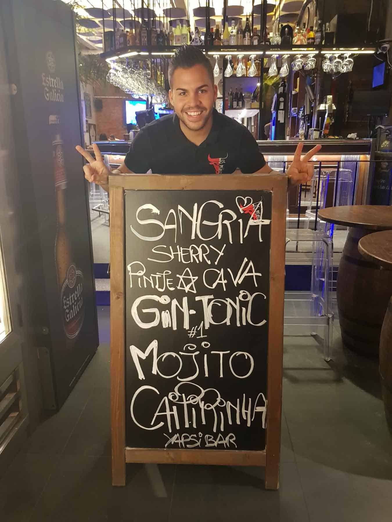 Un hombre alegre señala un colorido menú de cócteles en una pizarra en un restaurante o bar de moda.