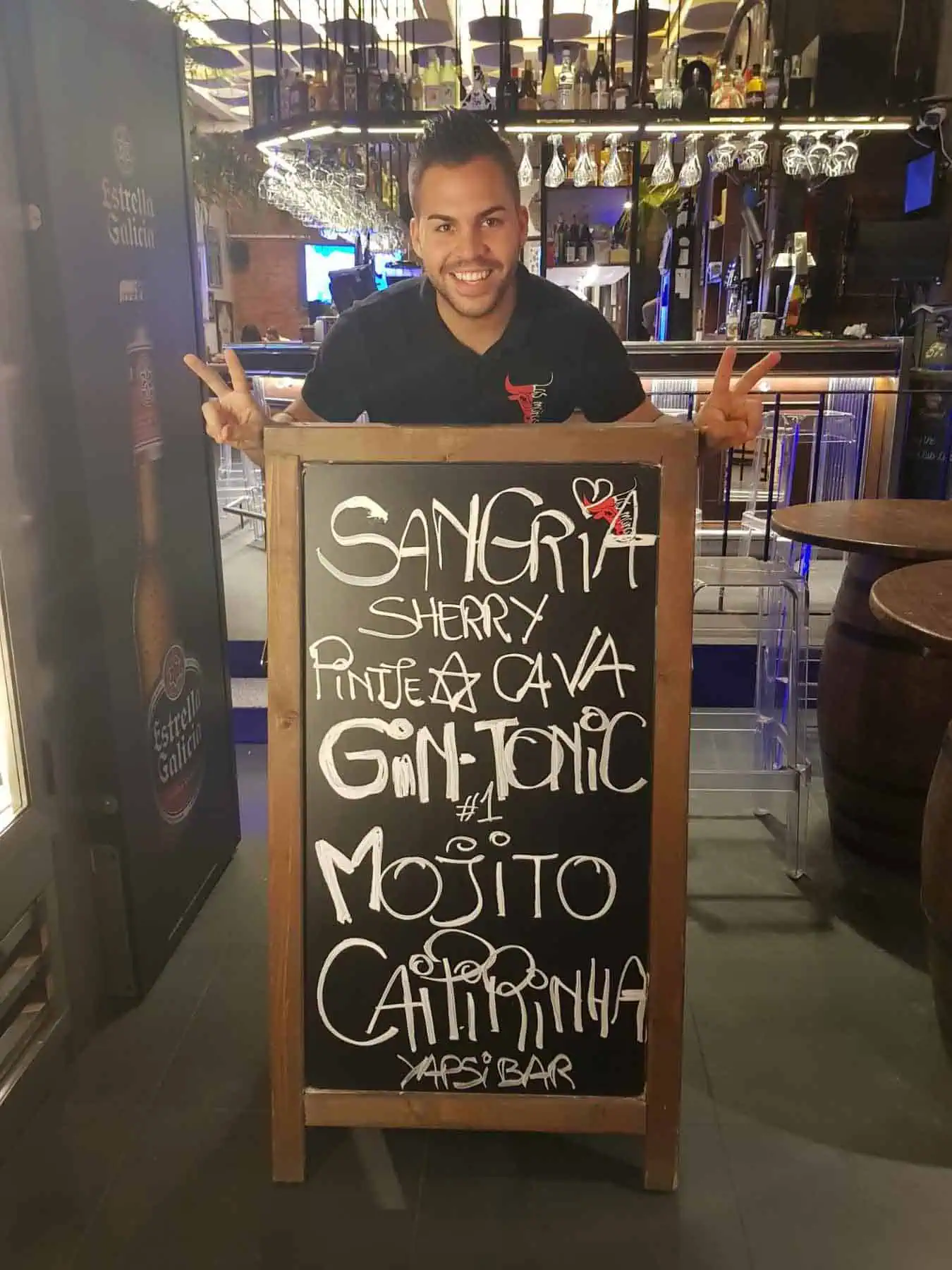 Een vrolijke man wijst naar een kleurrijk cocktailmenu op een krijtbord in een trendy restaurant of bar.