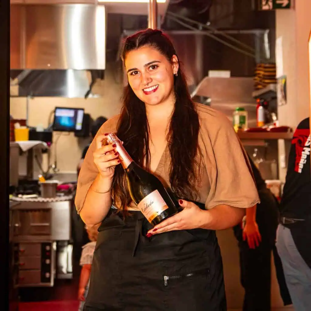 Champagne fles in hand, jonge vrouw serveert feestelijke sfeer in restaurant Las Mañas, Antwerpen, met warme ambiance en professionele service.
