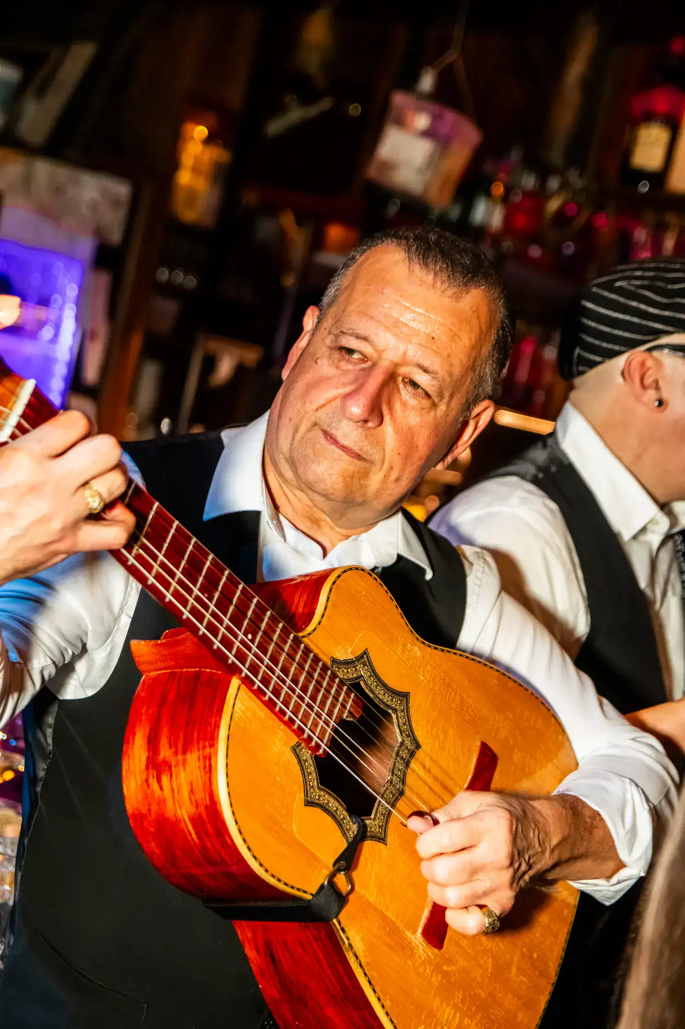 Un músico de Las Mañas Kings toca la guitarra en un bar de ambiente rodeado de otros músicos y un ambiente cálido.